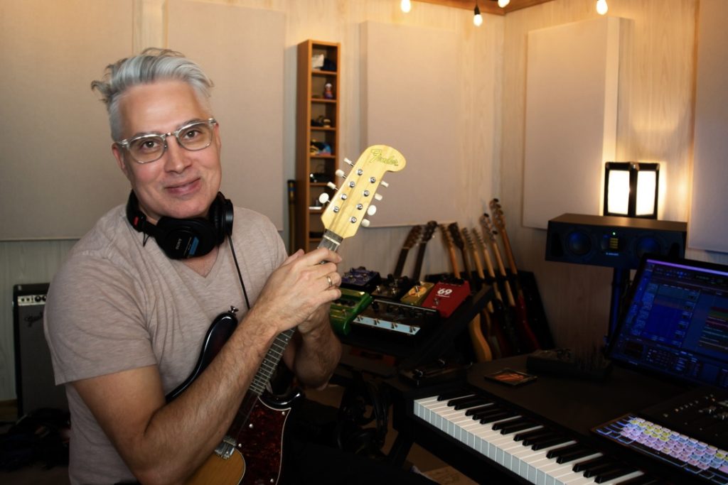 Composer Antonio Romero at his recording studio, holding a Fender electric mandolin